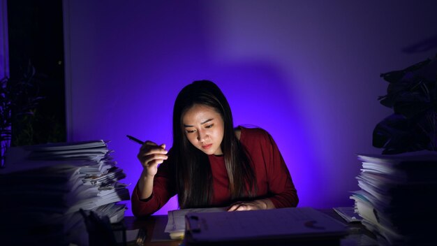 Une femme d'affaires asiatique qui travaille dur jusqu'à tard avec beaucoup de documents à la maison occupée et épuisée par les heures supplémentaires de travail la nuit