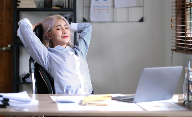 Femme d'affaires asiatique relaxante avec les mains derrière la tête et assise sur une chaise de bureau