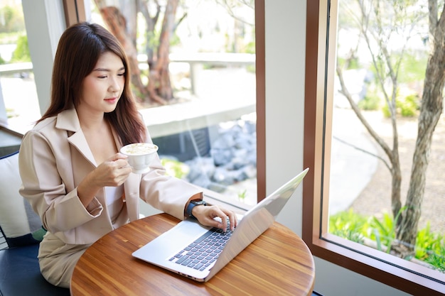 Femme d'affaires asiatique séduisante, boire du café et travailler par ordinateur portable dans le café Femme confiante et intelligente et concept d'entreprise