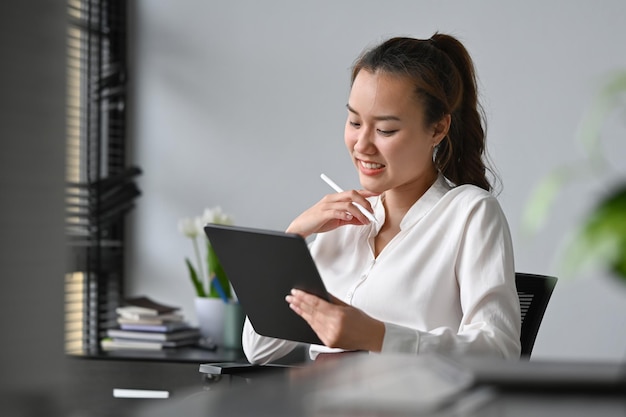 Femme d'affaires asiatique souriante recevant de bonnes nouvelles lisant des informations sur une tablette numérique