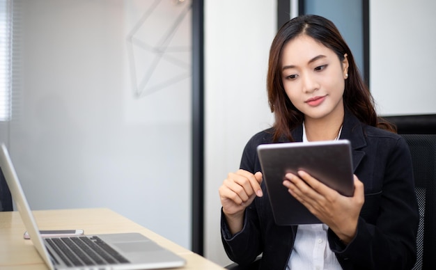 Femme d'affaires asiatique souriante utilisant une tablette pour le travail et jolie fille à la recherche de données et se concentrer sur sa tablette dans son bureau