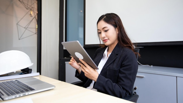 Femme d'affaires asiatique souriante utilisant une tablette pour le travail et jolie fille à la recherche de données et se concentrer sur sa tablette dans son bureau