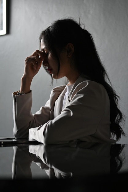 Femme d'affaires asiatique stressée et déprimée à son bureau dans la salle de bureau sombre