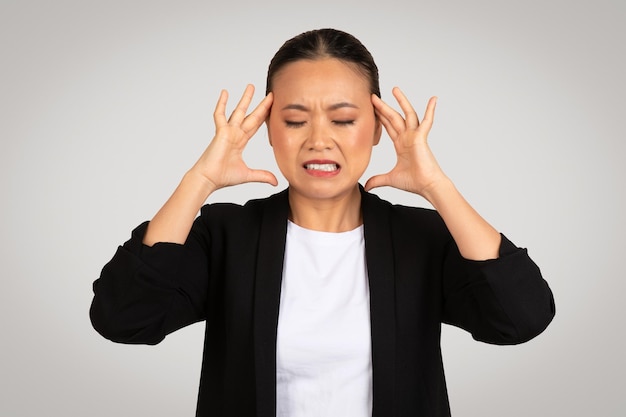 Femme d'affaires asiatique stressée avec une expression douloureuse tenant sa tête de frustration ou de maux de tête
