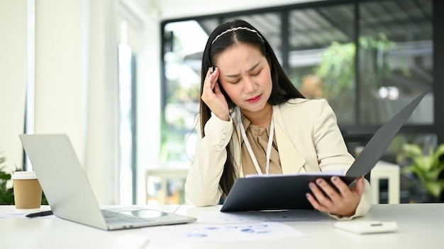 Femme d'affaires asiatique stressée lisant et examinant des rapports d'activité