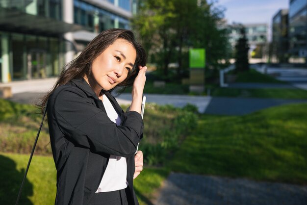 Femme d'affaires asiatique surmenée fatiguée en costume avec ordinateur portable en plein air