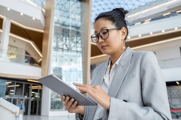 Femme d'affaires asiatique avec tablette faisant défiler les données en ligne