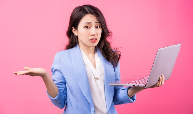 Femme d'affaires asiatique tenant un ordinateur portable sur rose