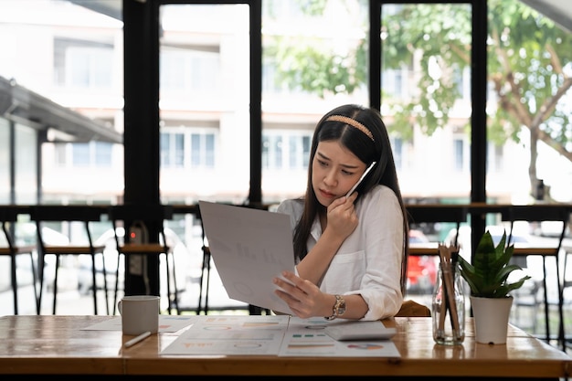 Femme d'affaires asiatique travaillant avec une calculatrice de paperasse au bureau tout en parlant au téléphone