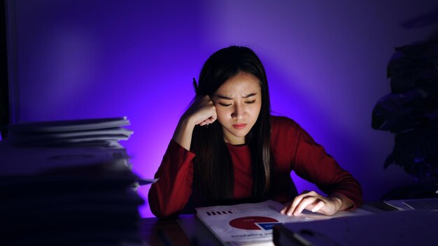 Femme d'affaires asiatique travaillant dur tard avec beaucoup de documents à la maison. Occupé et épuisé par les heures supplémentaires de travail la nuit.