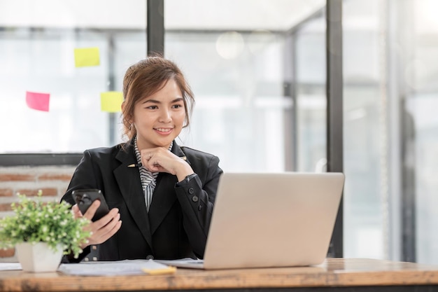 Photo une femme d'affaires asiatique utilisant un smartphone pour faire du travail de comptabilité avec un ordinateur portable et un graphique de rapports financiers au bureau