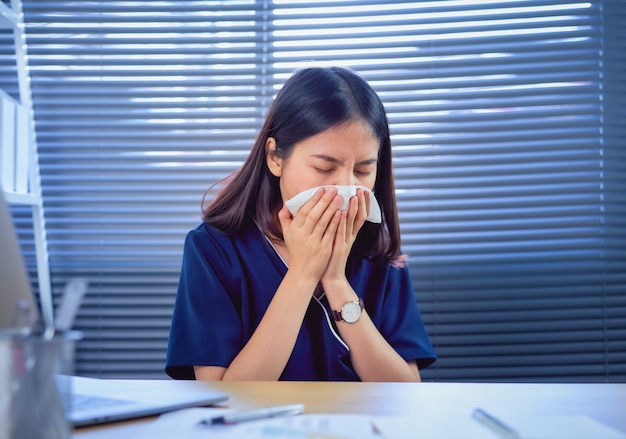 Femme d'affaires asiatique utilise une serviette en papier la bouche et le nez parce que l'allergie dans la table sur la salle de bureau.