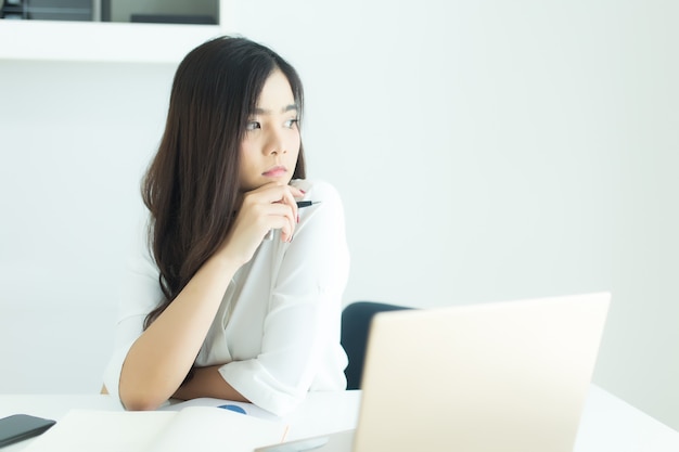 Femme d&#39;affaires asiatiques jeunes souriant et pensant idée de travailler au bureau de bureau moderne.