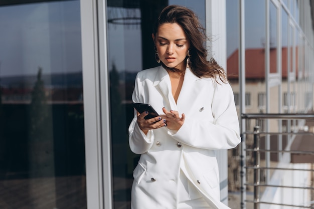 Femme d&#39;affaires assez élégant se dresse sur le balcon près du bureau moderne et parle sur le smartphone.