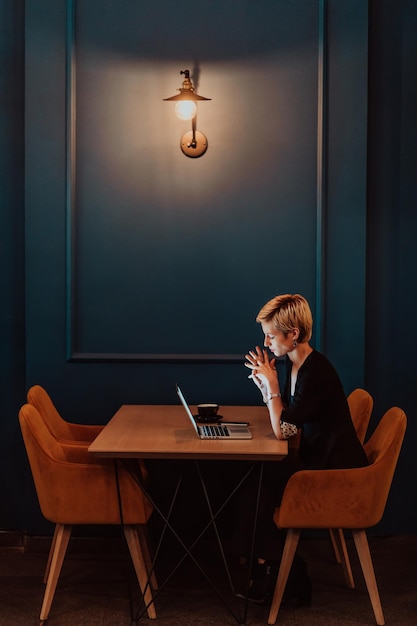 Une femme d'affaires assise dans un café à une table en bois buvant du café et utilisant un ordinateur portable Une femme daffaires navigant sur Internet, discutant, bloggeant Focus sélectif