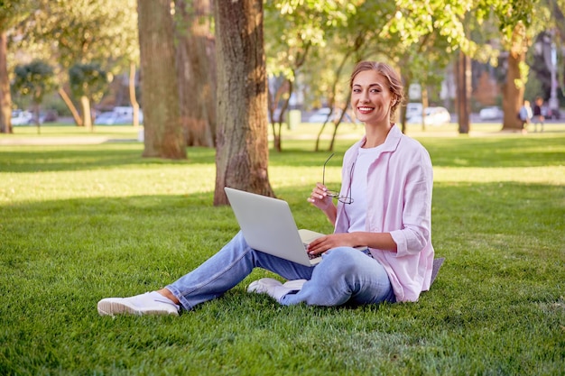 Femme d'affaires assise dans un parc d'été avec un ordinateur portable