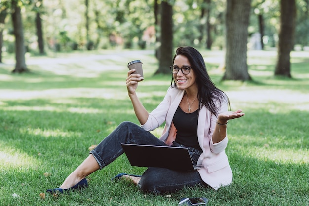 Femme d'affaires assise dans le parc d'herbe d'été à l'aide d'un ordinateur portable.