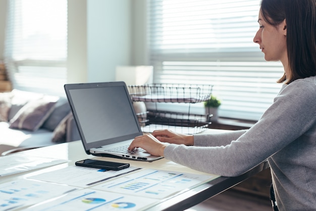 Femme d'affaires assise sur son lieu de travail au bureau, tapant, regardant l'écran d'un ordinateur portable.