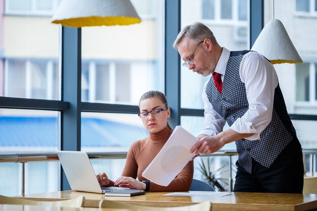 Une femme d'affaires assise à une table en bois avec un ordinateur portable et un mentor de patron d'enseignant qui travaille indique ses erreurs. École d'un nouveau concept de développement des affaires.