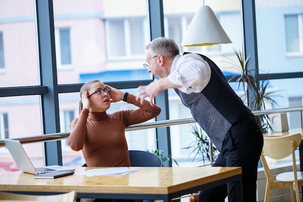 Une femme d'affaires assise à une table en bois avec un ordinateur portable et un mentor de patron d'enseignant qui travaille indique ses erreurs. Crie et frappe la table avec sa main