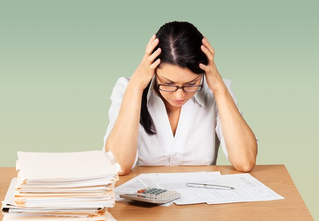 Femme d'affaires assise à la table avec de nombreux papiers au bureau