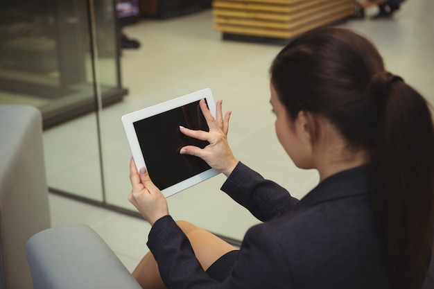 Femme d'affaires attentive assis sur un canapé et à l'aide de tablette numérique