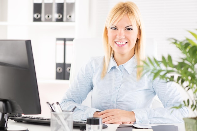 Femme d'affaires au bureau. Assis à la table avec ordinateur et regardant la caméra.