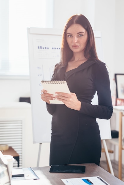 Femme d'affaires au bureau debout à son bureau avec un bloc-notes.