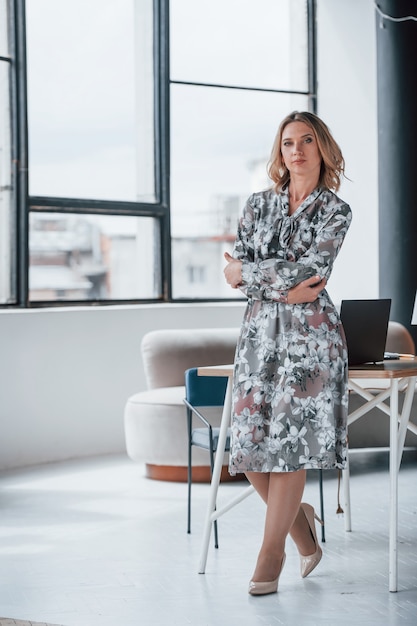 Femme d'affaires aux cheveux blonds bouclés debout dans la chambre contre la fenêtre.