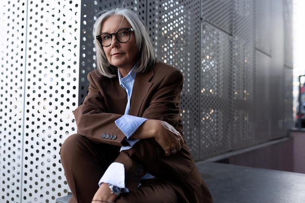 Une femme d'affaires aux cheveux gris d'un an, confiante, avec une coiffure bob, est vêtue d'une veste marron et