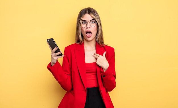 Femme d'affaires ayant l'air choquée et surprise avec la bouche grande ouverte, pointant vers soi. notion de smartphone