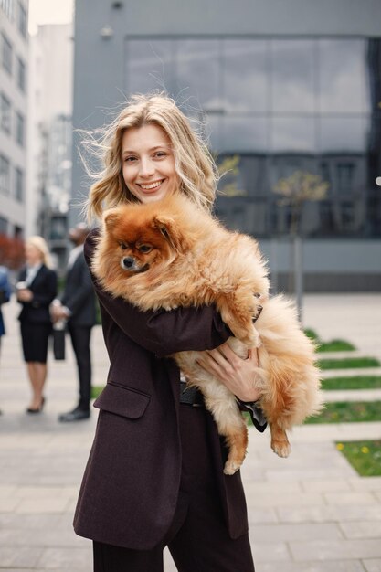 Femme d'affaires blonde debout et tenant un chien devant un bureau moderne