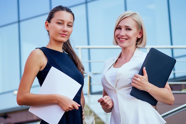 Femme d'affaires blonde et femme brune tenant des dossiers et des titres dans le fond de gratte-ciel de mains