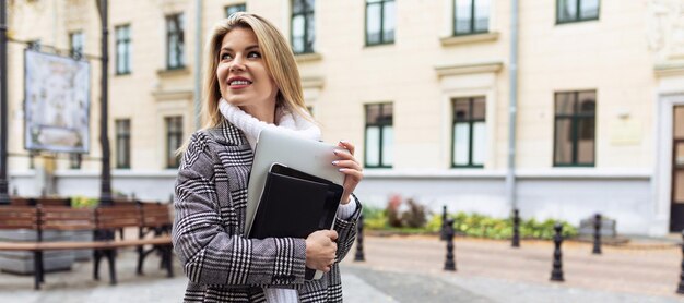 Femme d'affaires blonde avec un ordinateur portable dans ses mains sur le fond de la ville