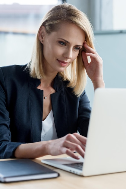 Femme d'affaires blonde souriante utilisant un ordinateur portable sur le lieu de travail