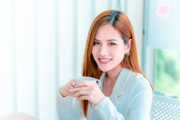 Femme d&#39;affaires, boire du café dans les fenêtres du bureau le matin