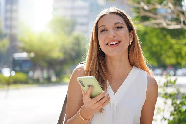 Femme d'affaires brésilienne confiante regardant la caméra à l'aide d'un smartphone à l'extérieur en été Espace de copie