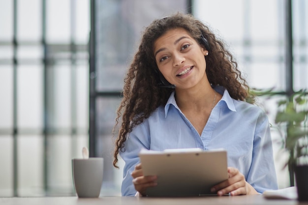 Femme d'affaires brune utilisant un casque pour communiquer et conseiller les gens dans le bureau du service client