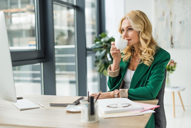 une femme d'affaires buvant du café et utilisant un ordinateur de bureau sur son lieu de travail