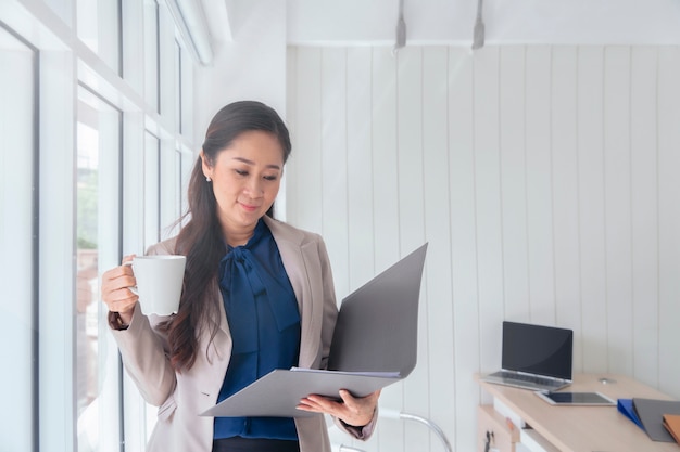 Femme d&#39;affaires buvant une tasse de café et debout devant une fenêtre de bureau