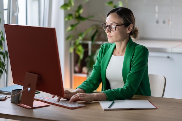 Une femme d'affaires caucasienne concentrée et réussie travaillant sur un ordinateur en tapant des e-mails est assise au bureau