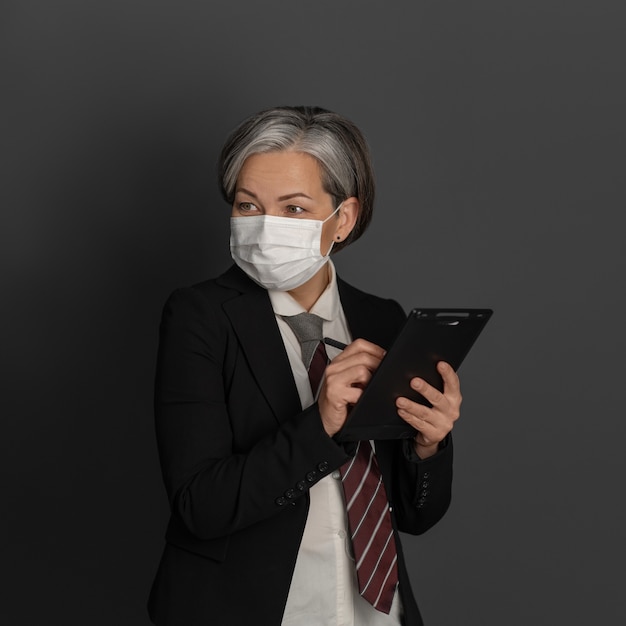 Femme d'affaires caucasienne masquée écrit avec un stylo en blanc tout en regardant sur le côté. Concept de quarantaine