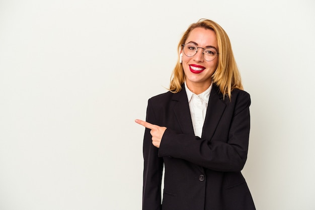 Femme d'affaires caucasienne portant un casque sans fil isolé sur fond blanc souriant et pointant de côté, montrant quelque chose dans un espace vide.