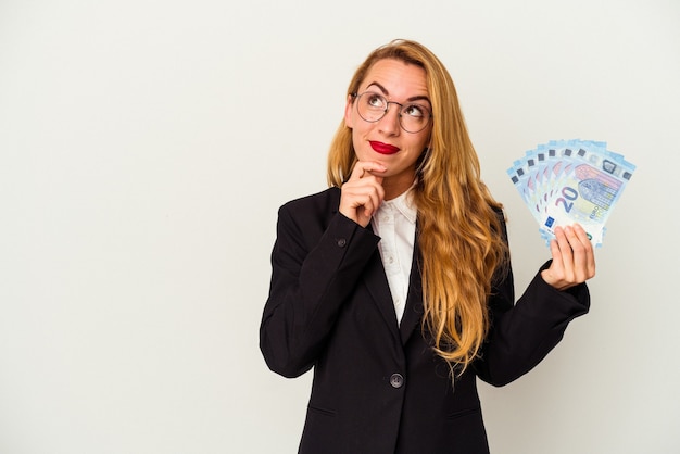 Femme d'affaires caucasienne tenant des factures isolées sur fond blanc regardant de côté avec une expression douteuse et sceptique.