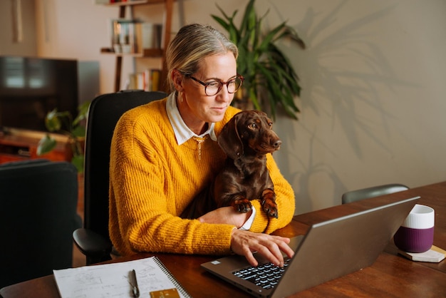 Femme d'affaires caucasienne travaillant à domicile tenant un chien sur ses genoux