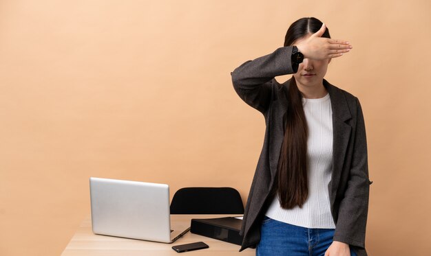 Femme d'affaires chinoise sur son lieu de travail couvrant les yeux par les mains