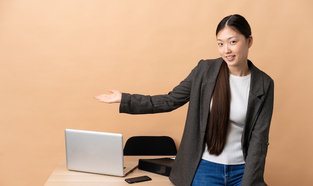 Femme d'affaires chinoise sur son lieu de travail tendant les mains sur le côté pour avoir invité à venir