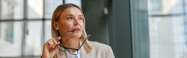 Femme d'affaires ciblée tenant des lunettes et regardant la fenêtre tout en travaillant dans un café moderne