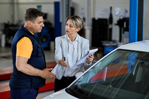 Femme d'affaires communiquant avec un réparateur automobile et lui donnant des instructions dans un atelier