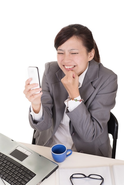 Femme d'affaires confiante à l'aide de téléphone portable et assis sur une chaise au bureau sur fond blanc.